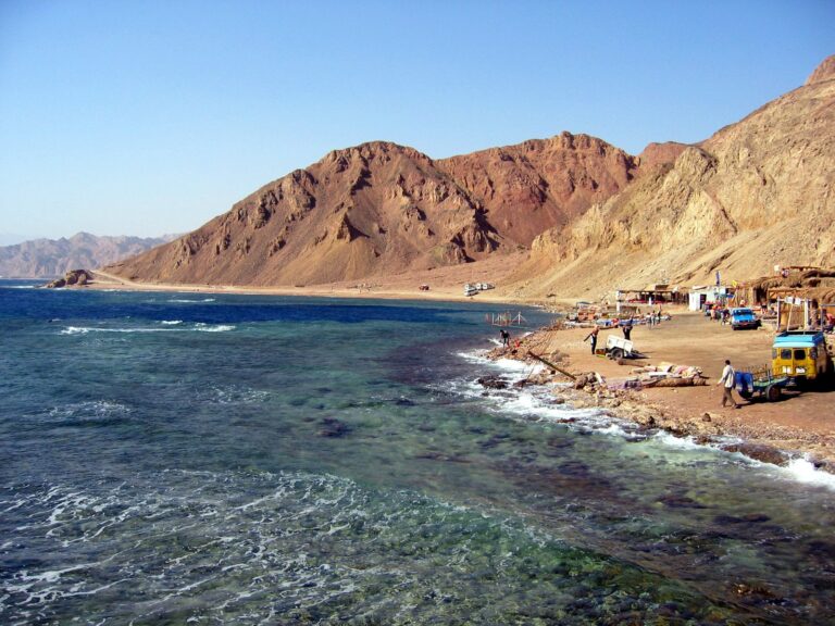 A peaceful scene of Dahab beach with colorful cushions and tents, framed by sun-drenched mountains